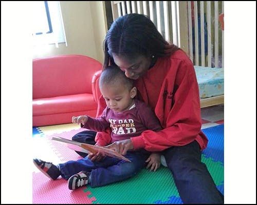 Person and child sitting on floor reading a book