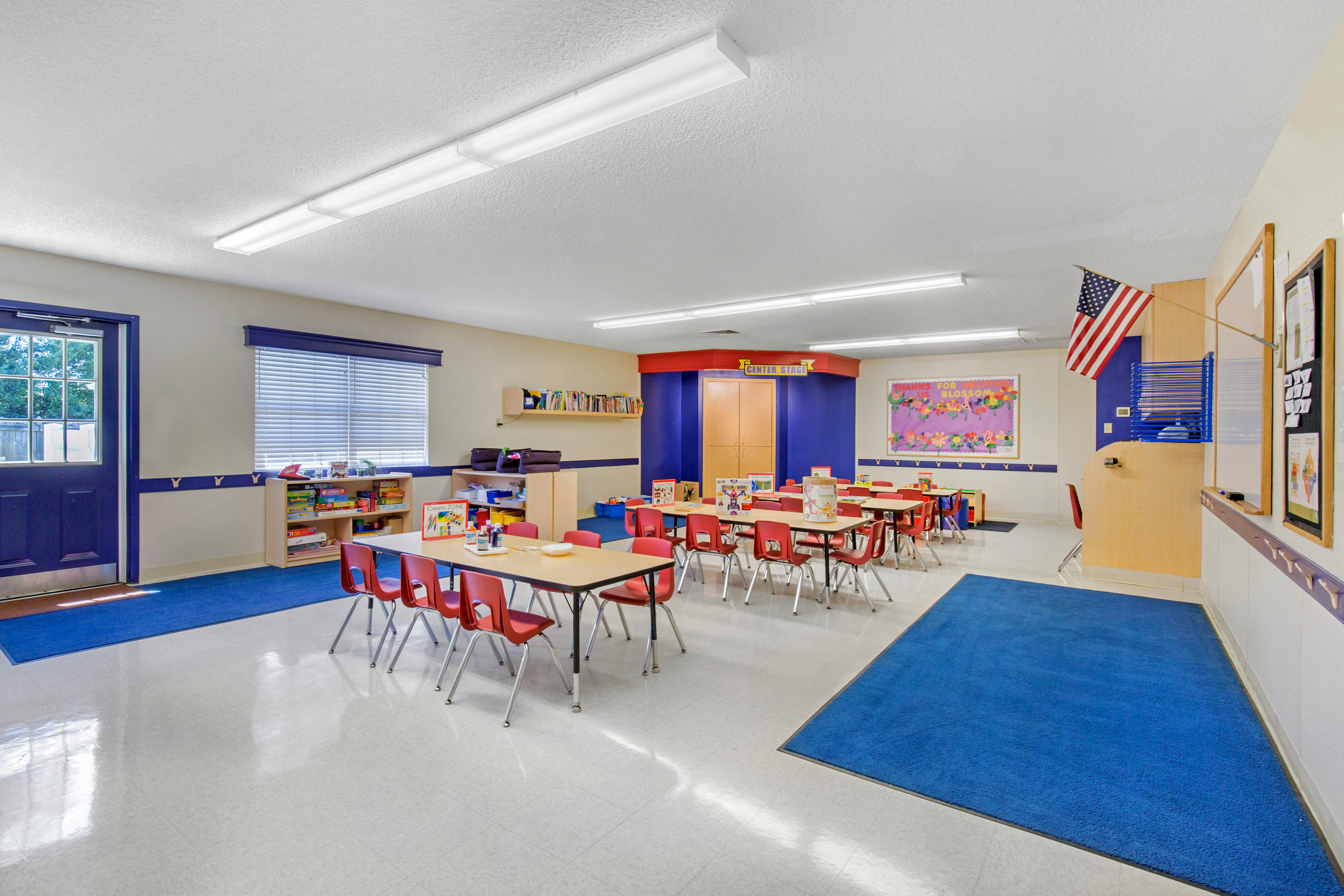 Classroom with small tables and red chairs, bookshelves, and an American flag