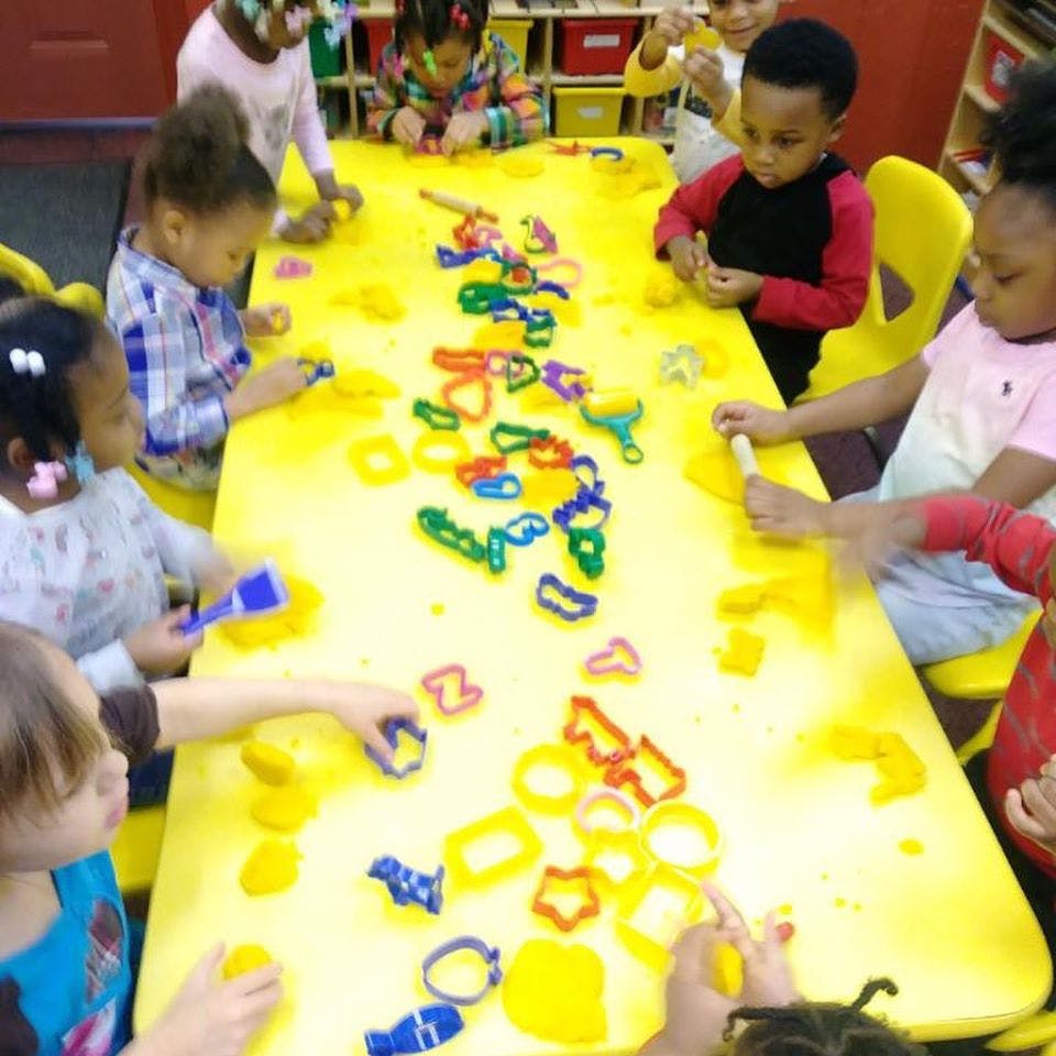 Children playing with colorful cookie cutters and yellow dough at a table