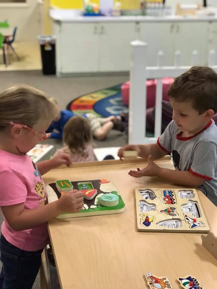 Two children playing with puzzles at a table in a classroom