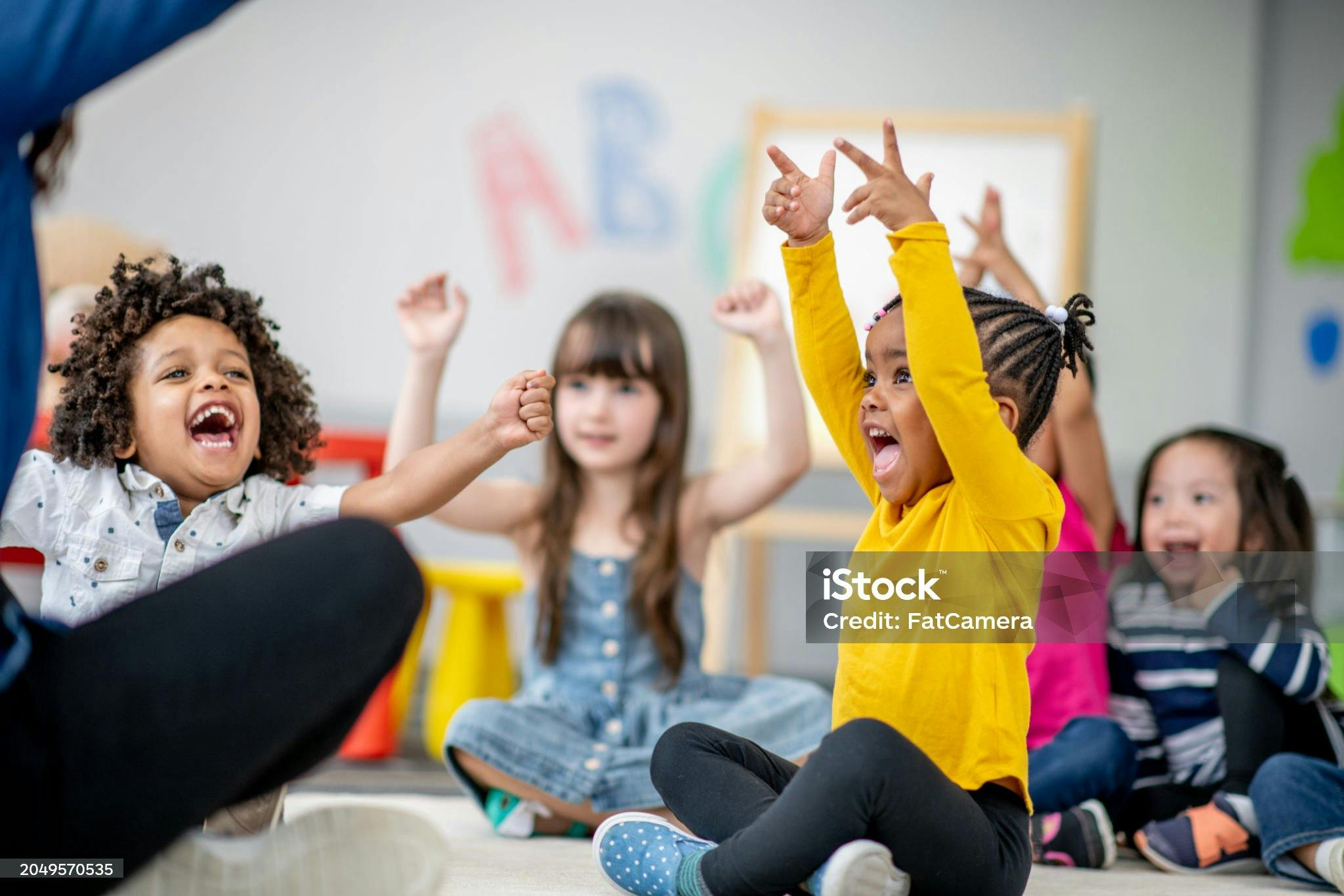 Children sitting on the floor with arms raised in a classroom