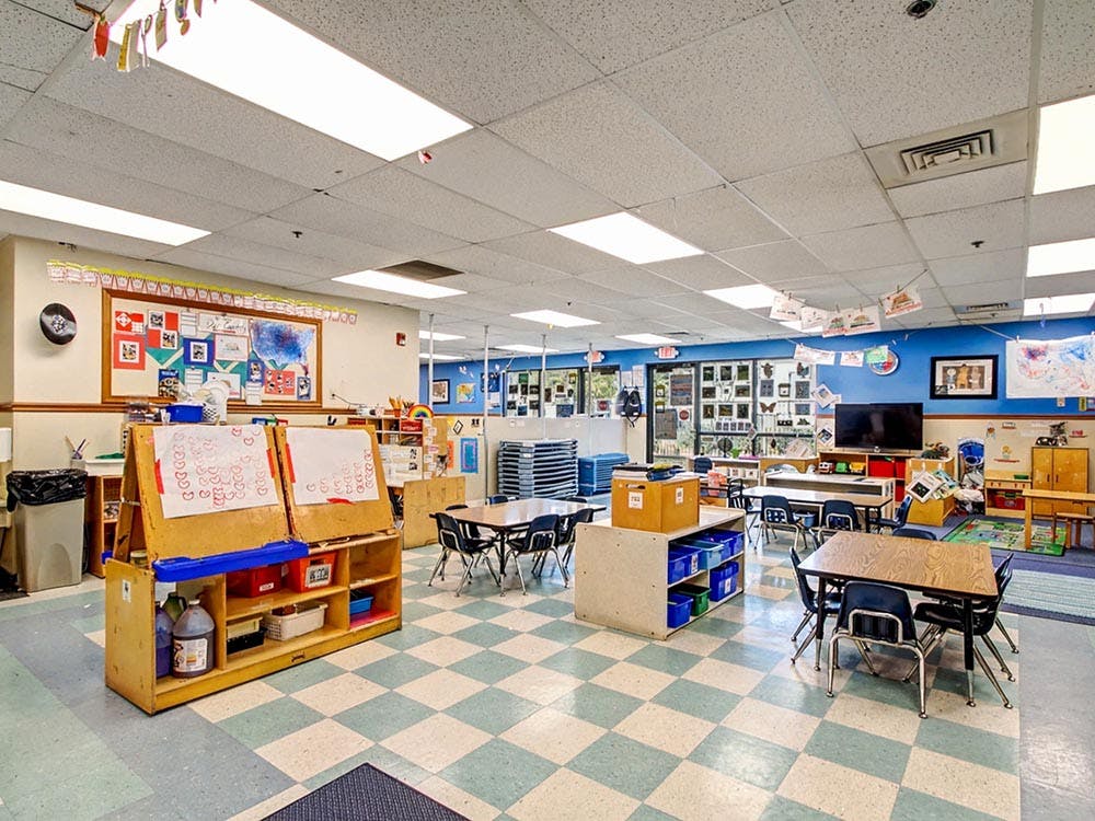 An empty classroom with small tables, chairs, and art supplies