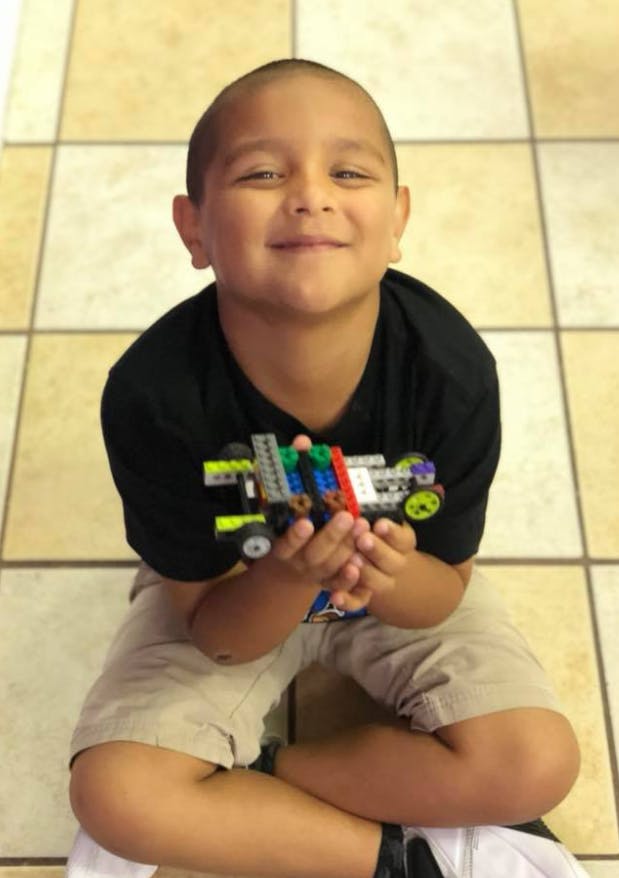 Child holding a toy car made of building blocks
