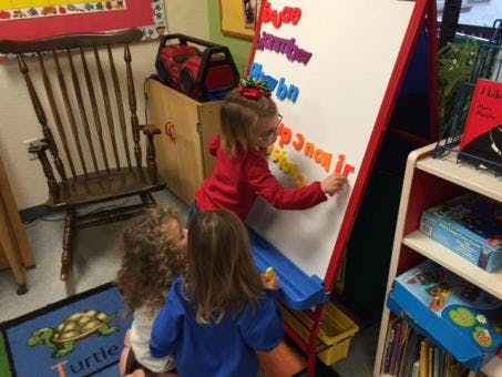 Three children playing with magnetic letters on a whiteboard in a classroom
