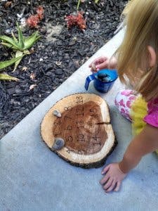 Child playing with a wooden tree slice with numbers and small rocks