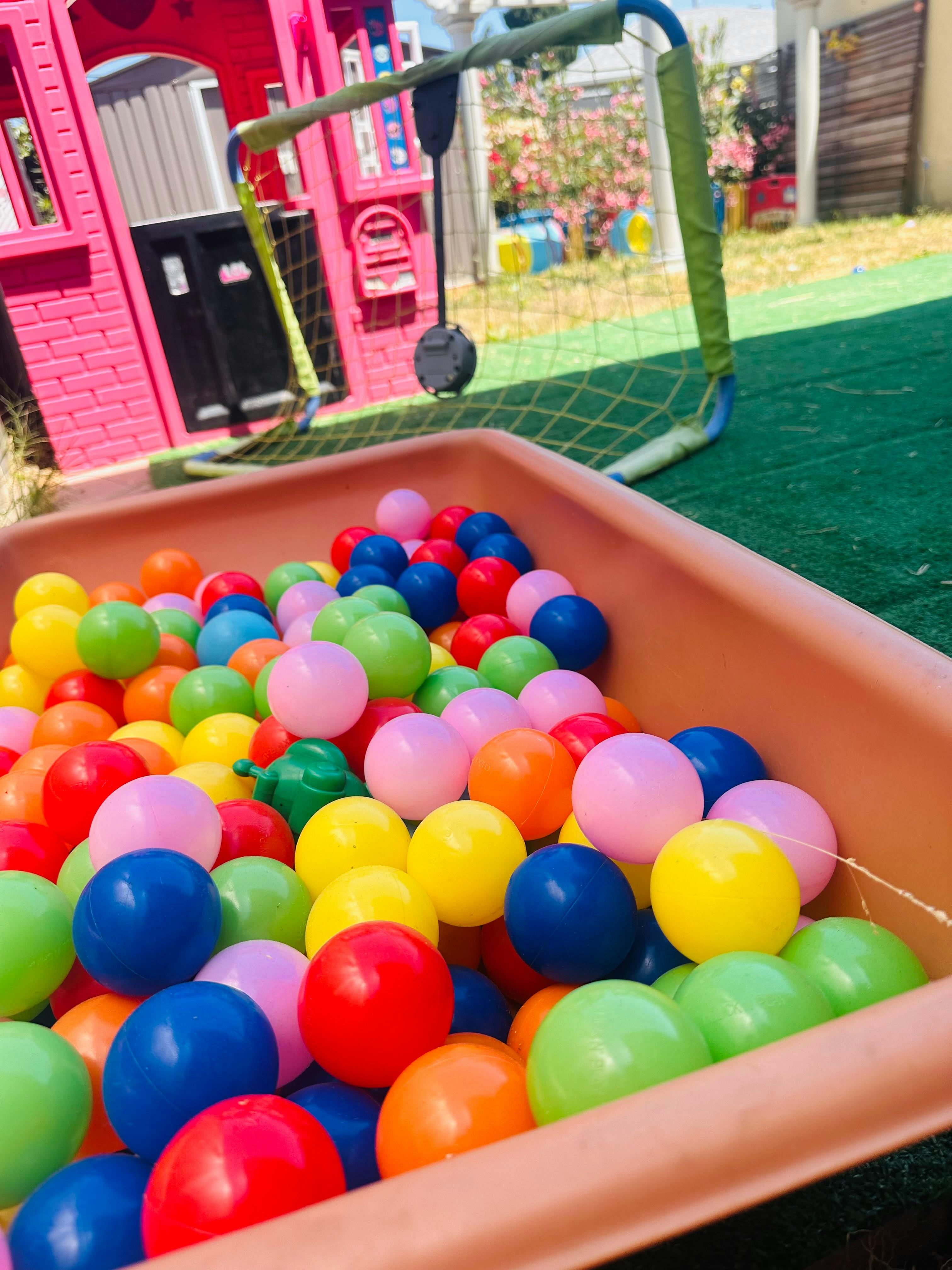 Colorful plastic balls in a brown bin with a playhouse and soccer goal in the background