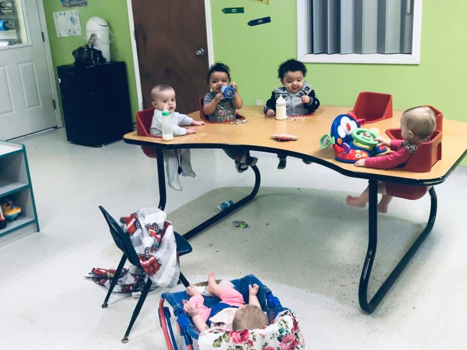 Four children sitting at a table with one child on the floor