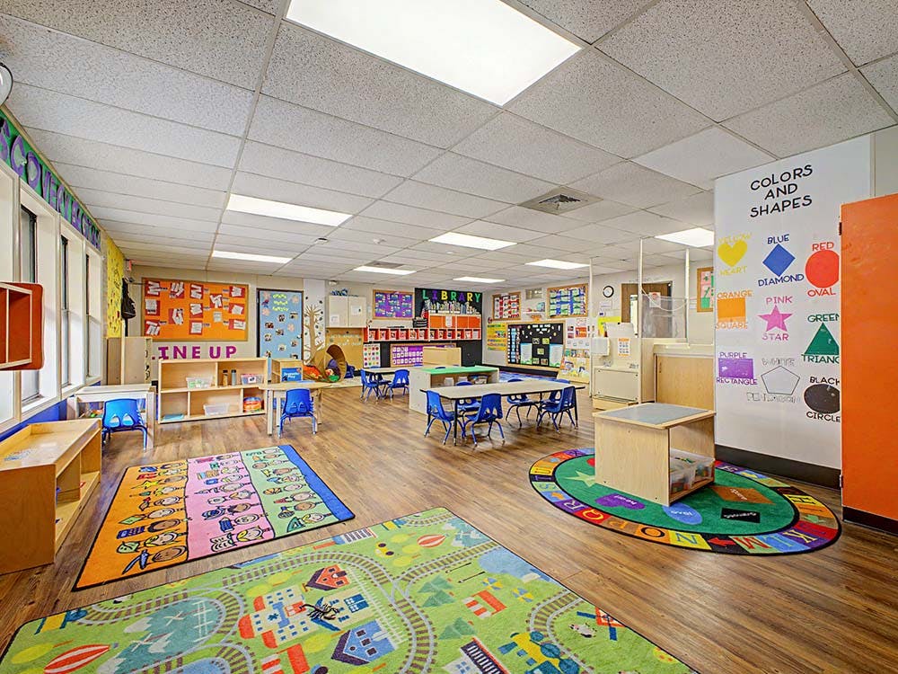 Empty classroom with colorful rugs, small tables, and educational decorations
