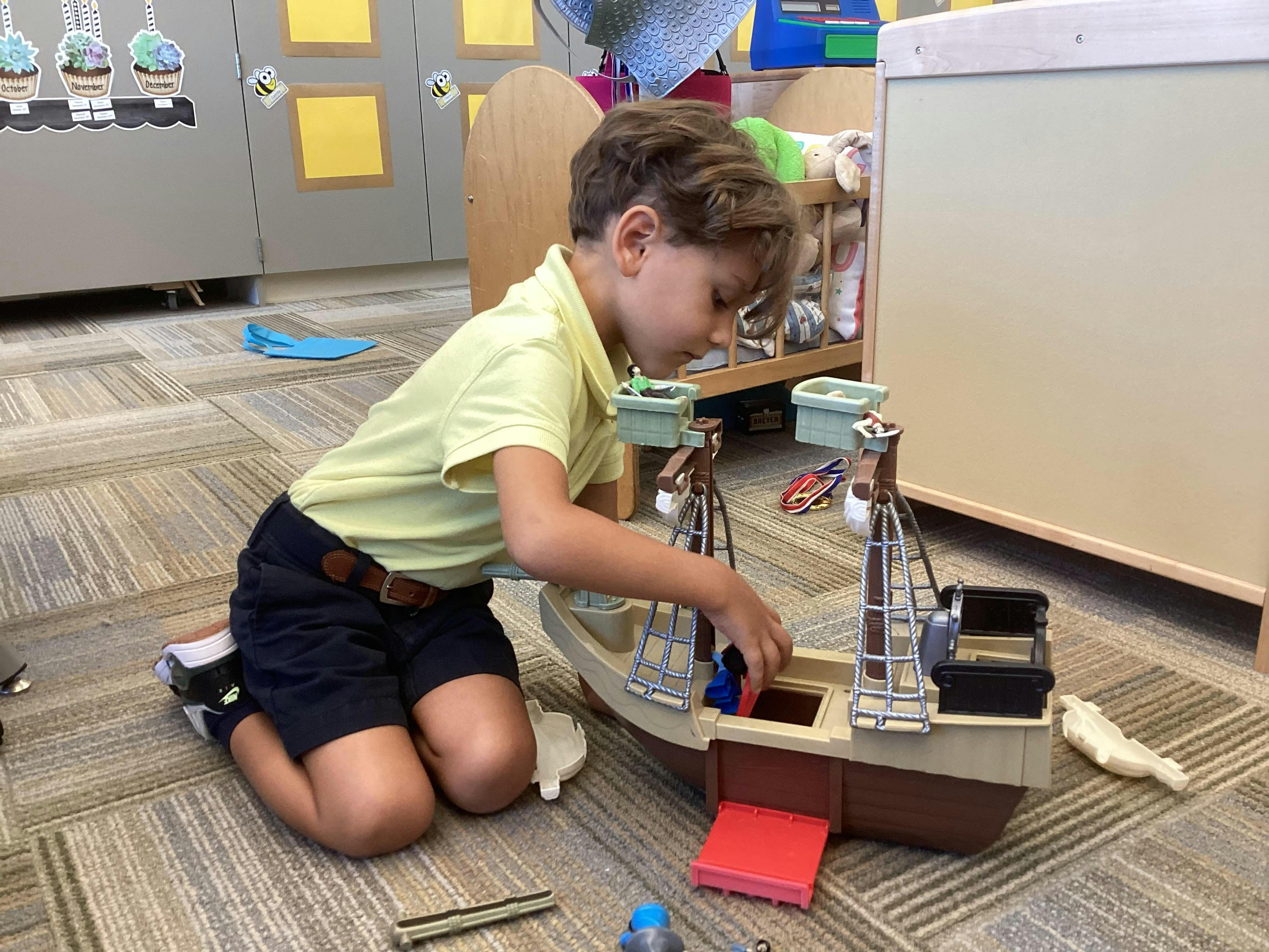 Child kneeling on floor playing with a toy boat