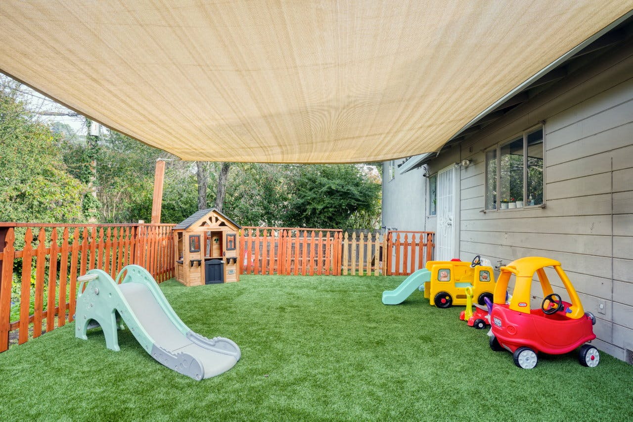 Outdoor play area with artificial turf, slides, playhouse, and toy cars