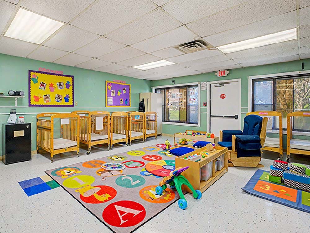 A nursery with cribs, play mats, toys, and a rocking chair
