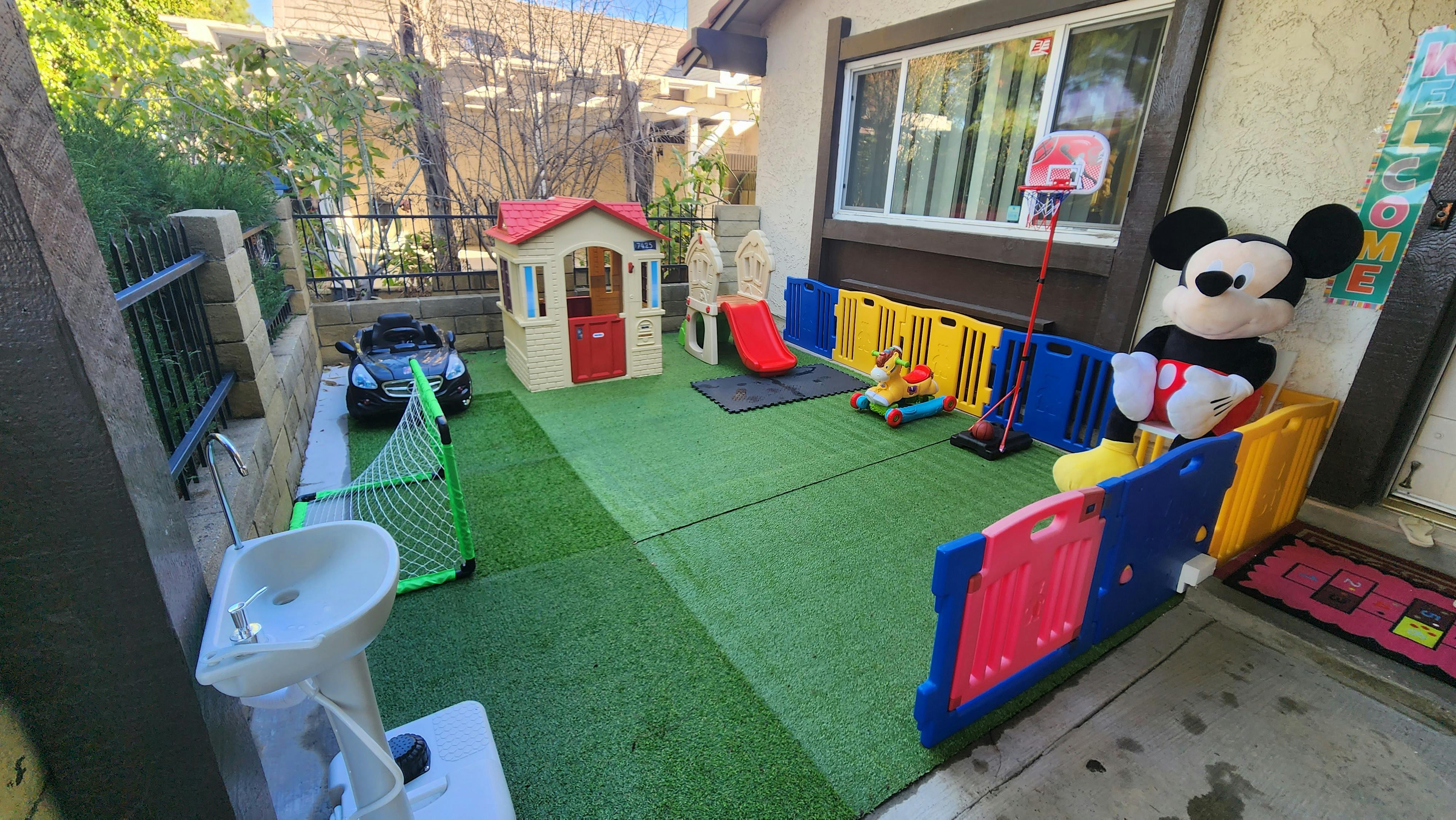 Outdoor play area with artificial turf, playhouse, toy car, and large Mickey Mouse plush