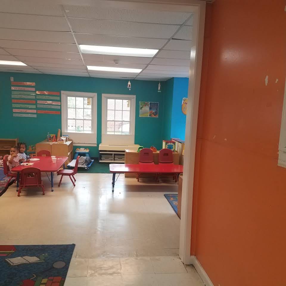 Classroom with red tables and chairs, two windows, and a child seated at a table
