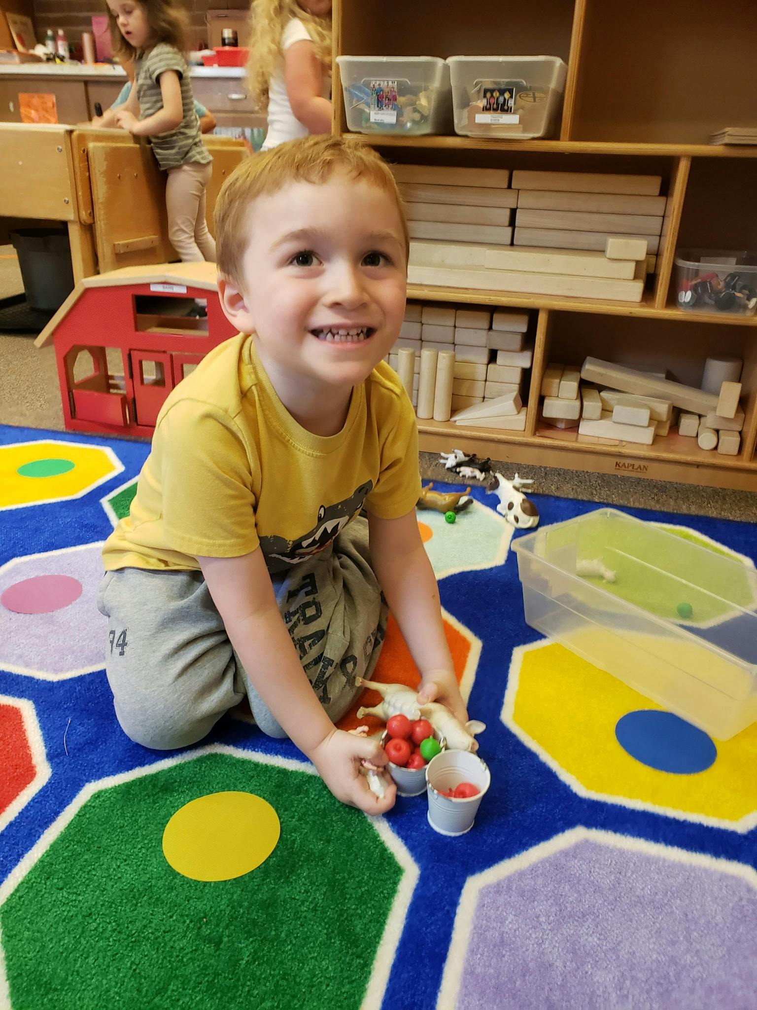 Child kneeling on a colorful rug, holding small red and green objects