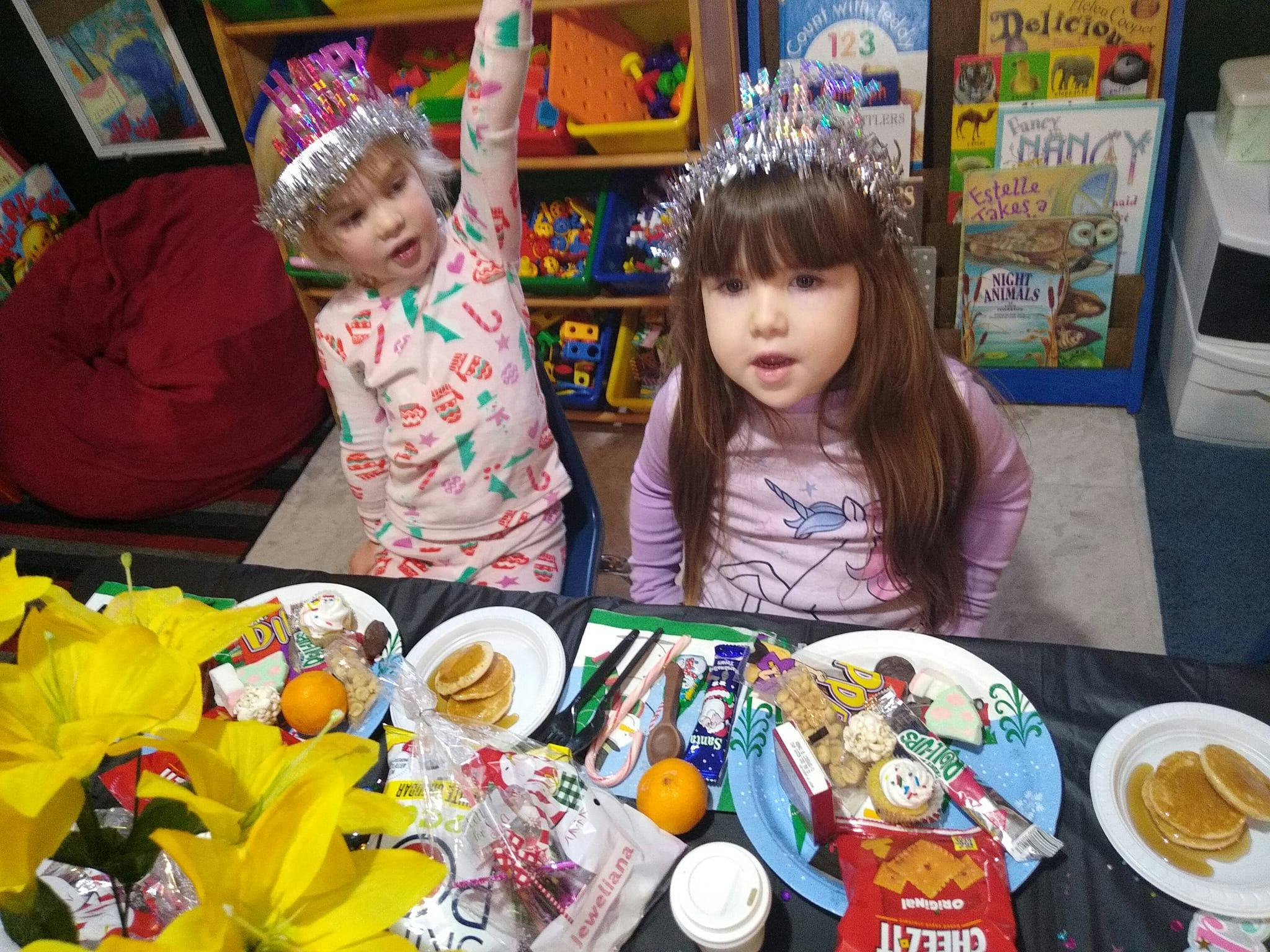 Two children wearing crowns sitting at a table with plates of food