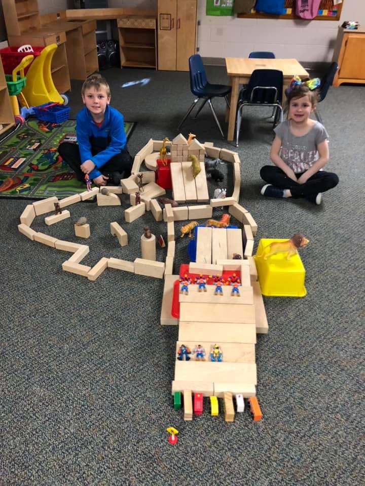 Two children sitting on the floor with a large block structure