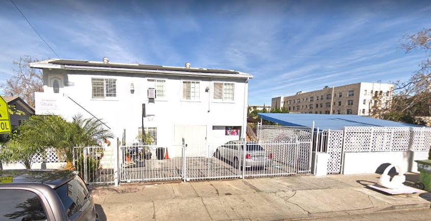 White two-story building with a gated parking area and blue awning