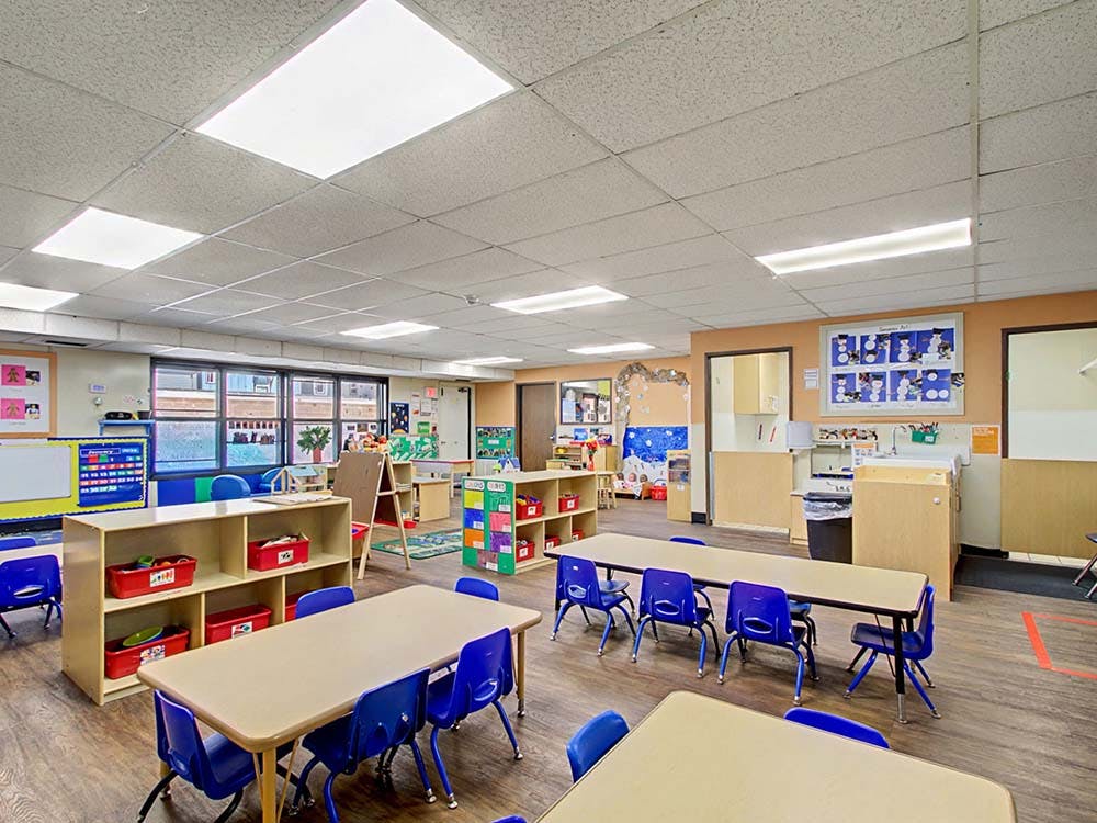 Empty classroom with tables, chairs, and shelves of learning materials