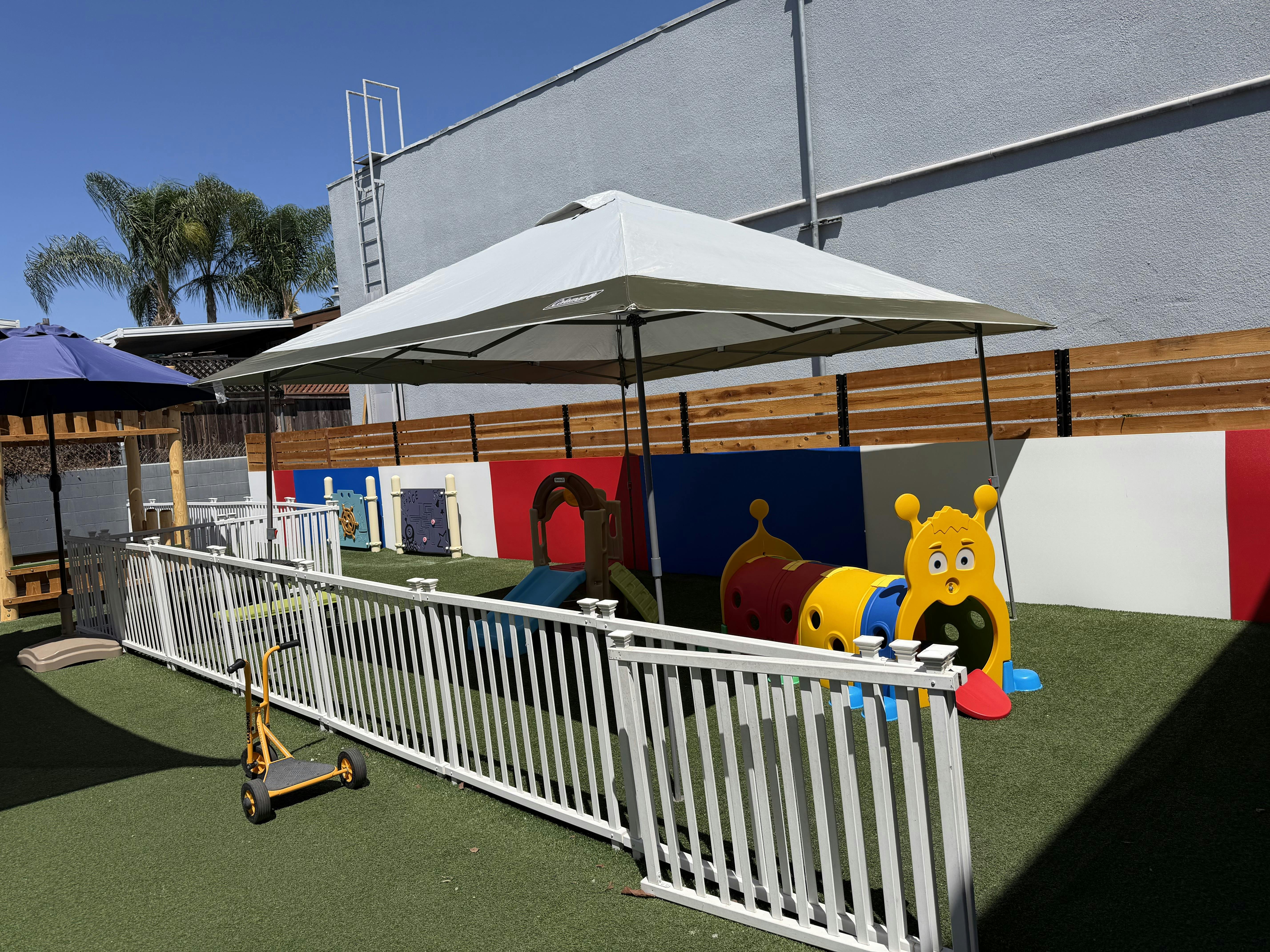 Playground area with plastic play equipment and a canopy tent on artificial grass