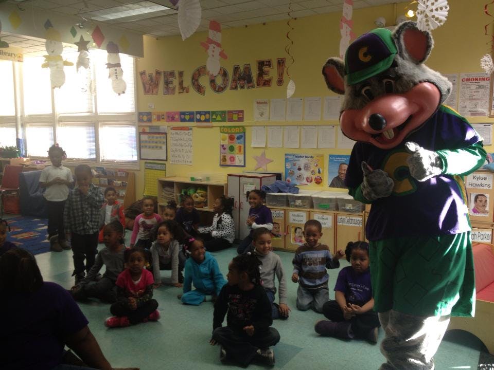 Mascot character standing in front of children sitting on the floor in a classroom