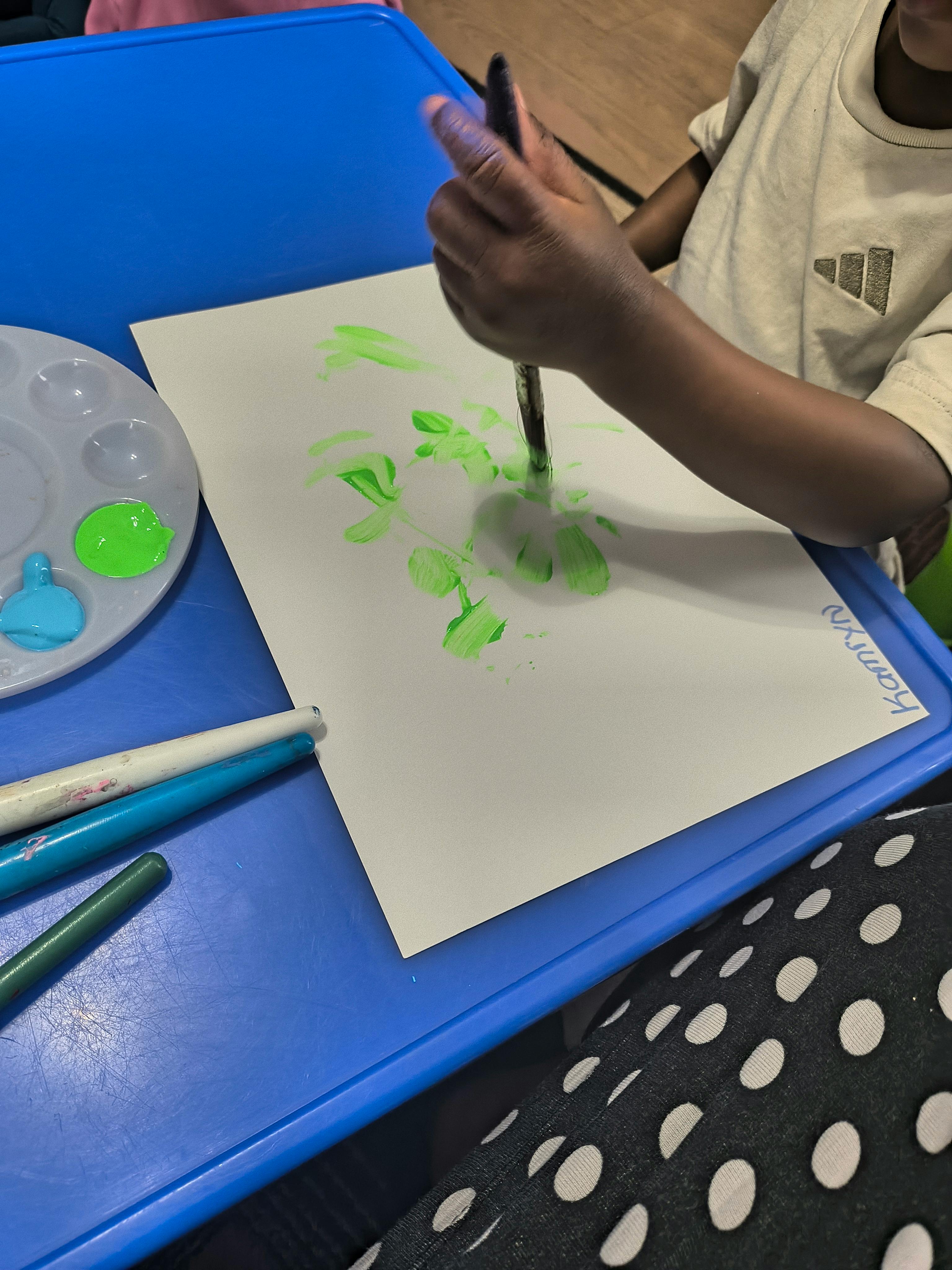 Child painting green shapes on paper with a paintbrush