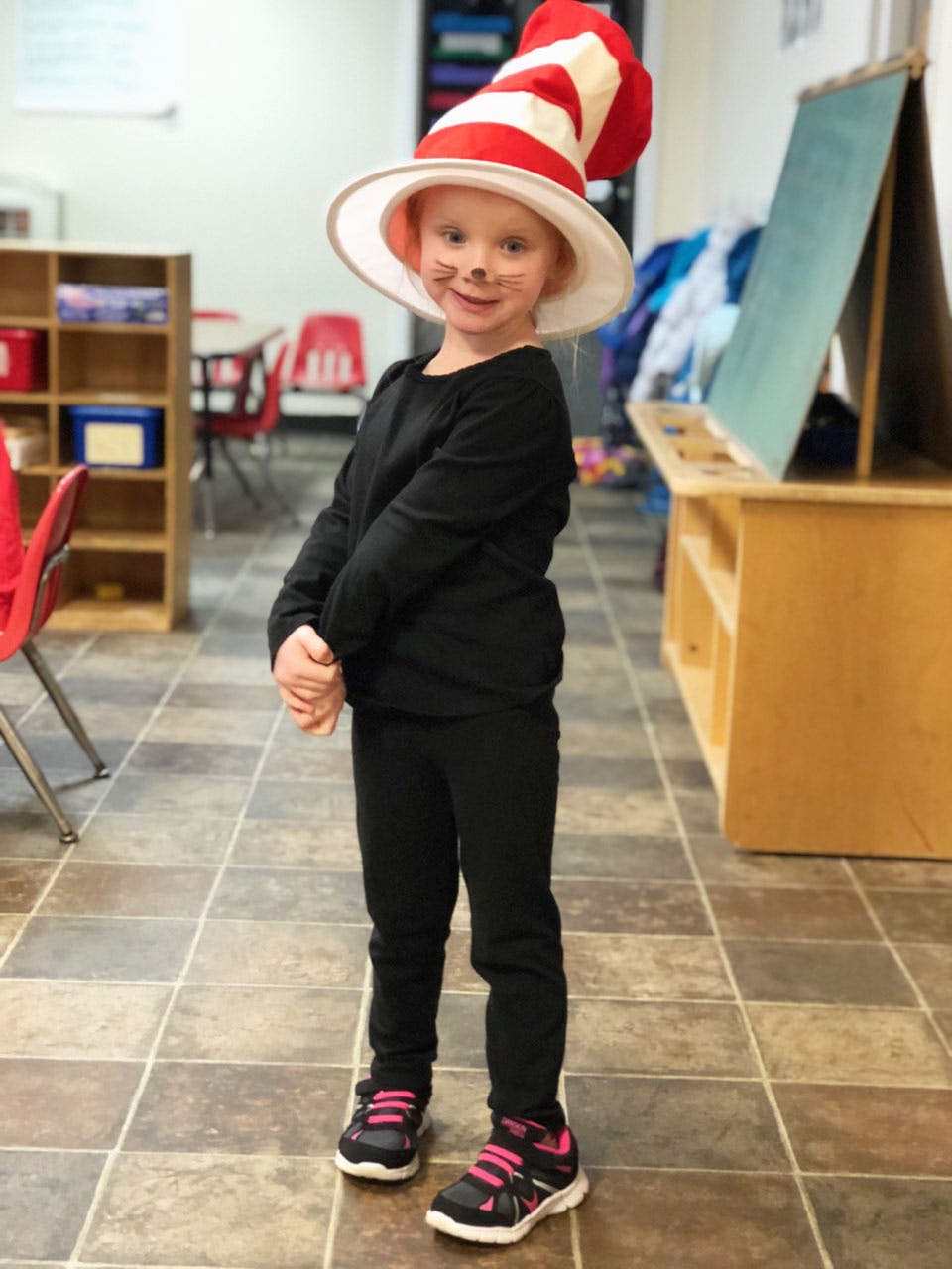 Child in a red and white striped hat with whiskers drawn on their face