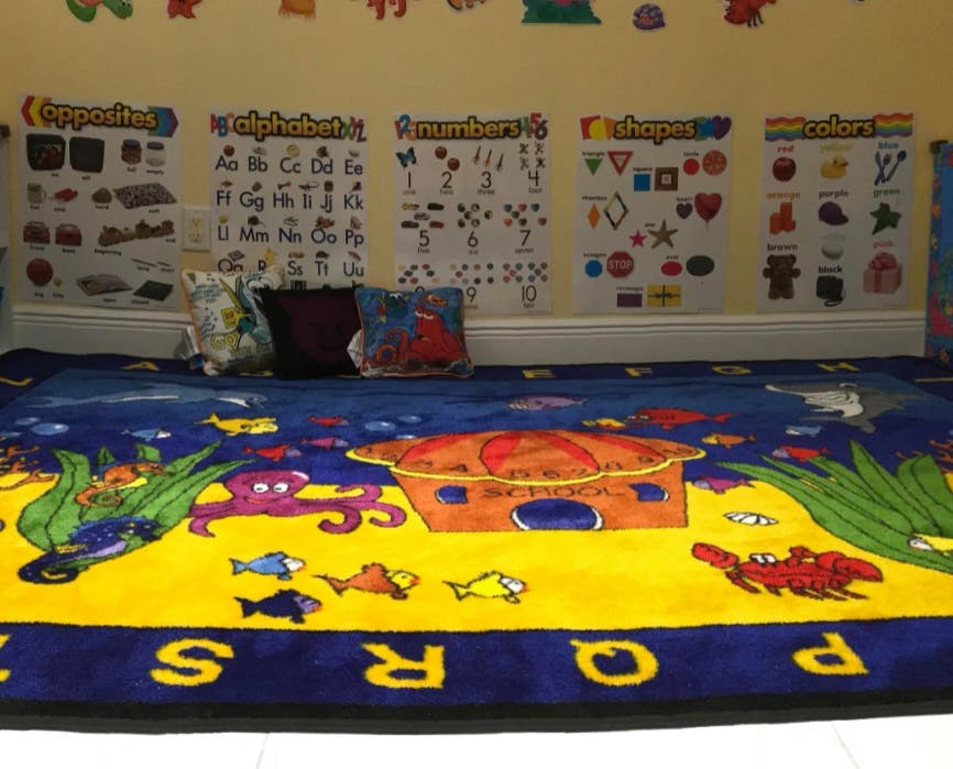 Classroom with an alphabet and numbers rug and shapes posters above a colorful rug