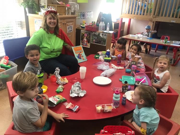 Adult and multiple children sitting around a red table in a classroom