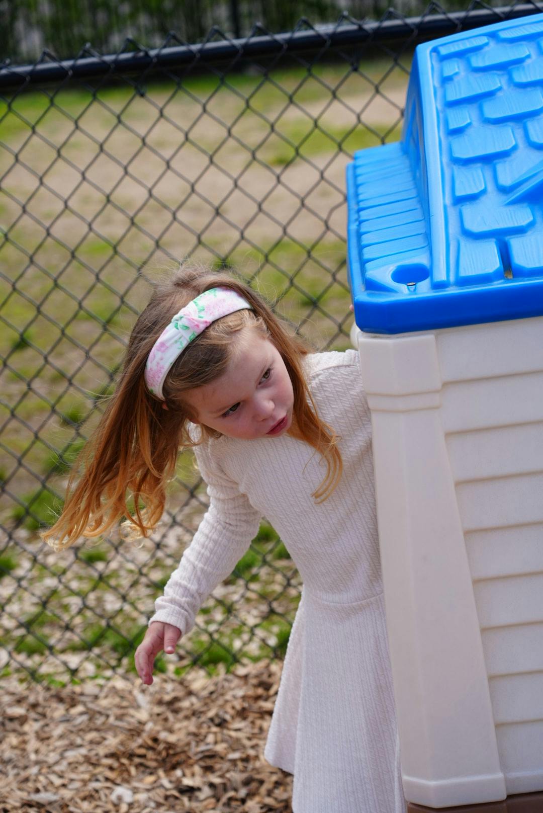 Child wearing a white dress and headband, on top of a play structure