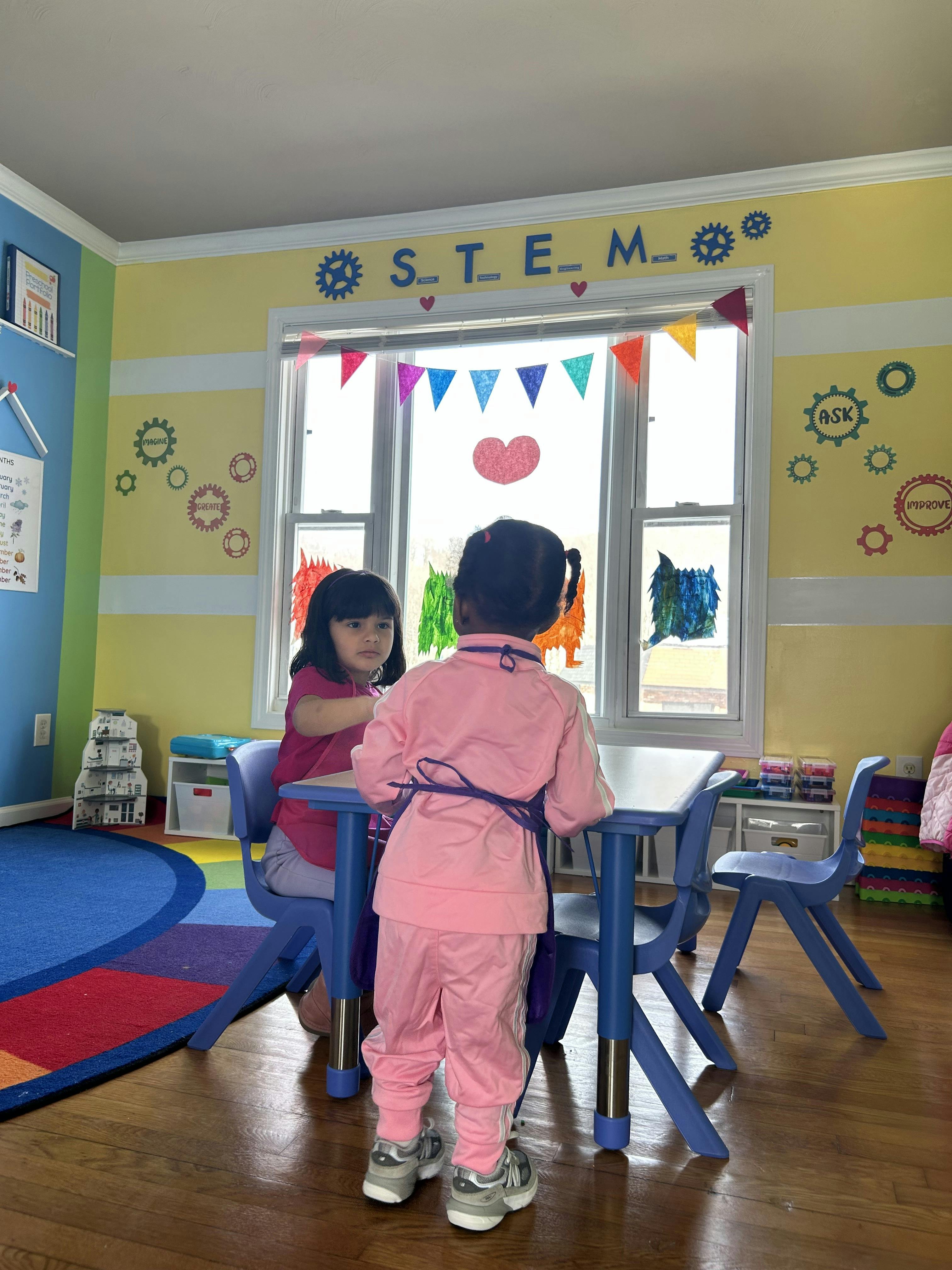 Two children at a blue table in a classroom with STEM decorations