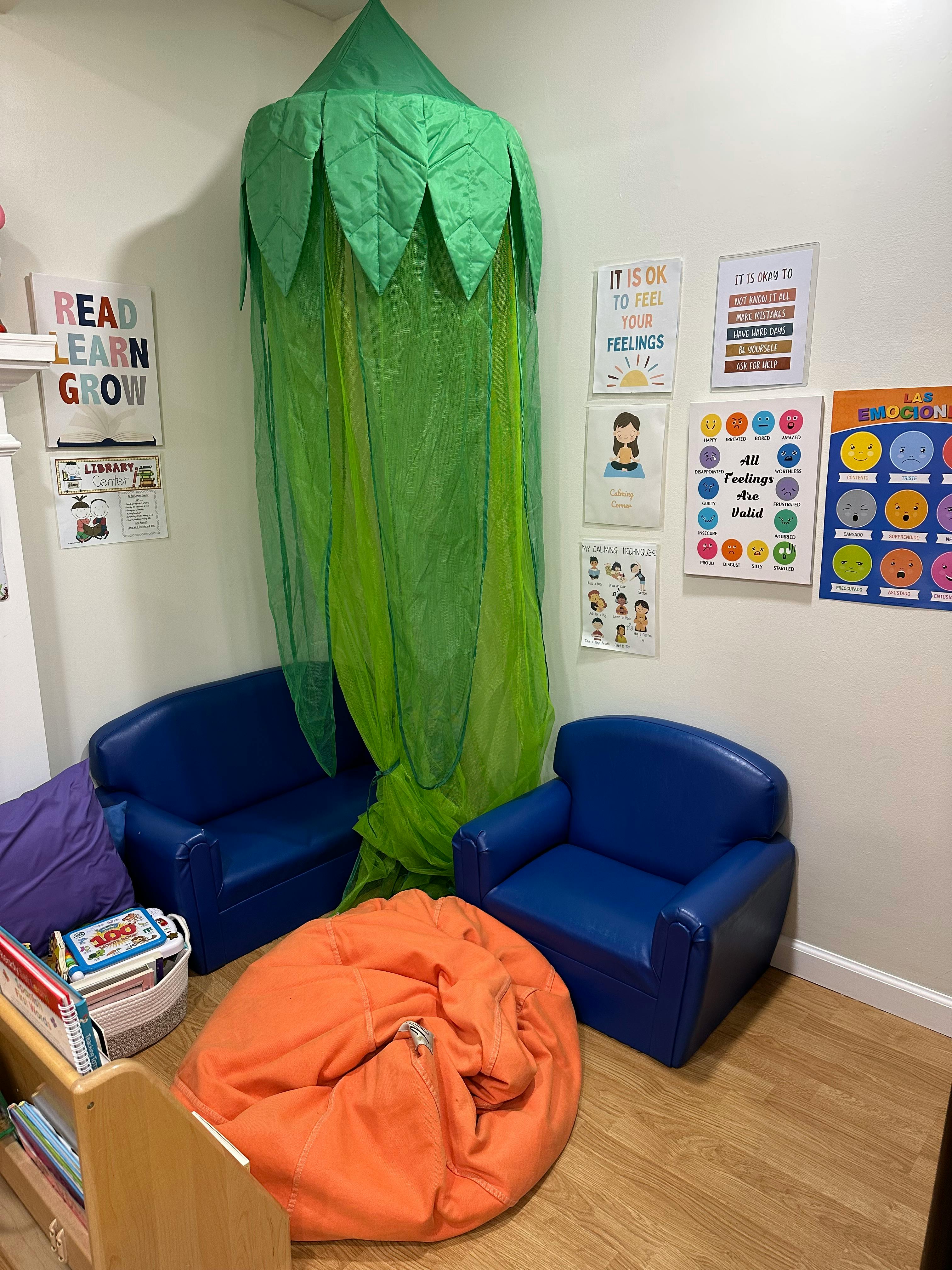 Children's reading nook with blue chairs, orange beanbag, and green canopy