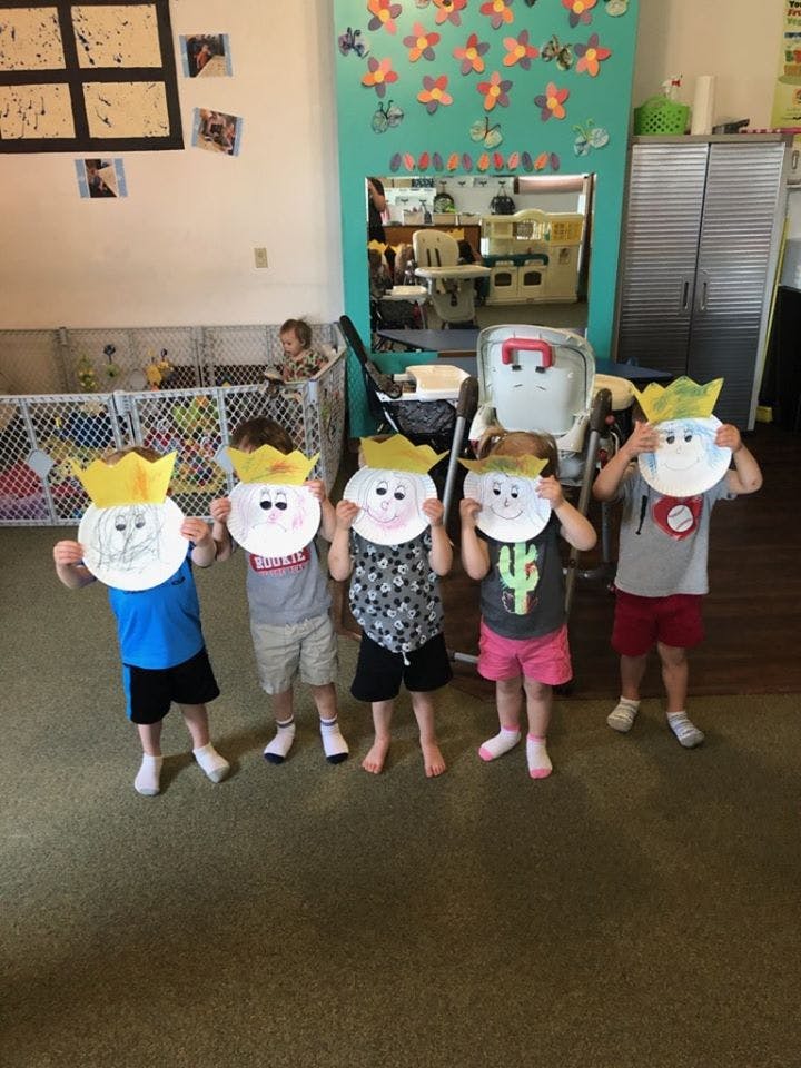 Five children holding up paper plate masks with crowns