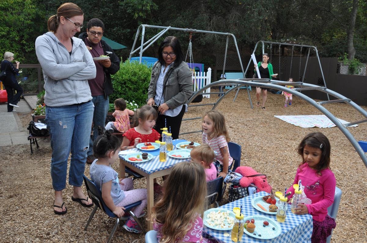 Adults and children gathered around tables outdoors
