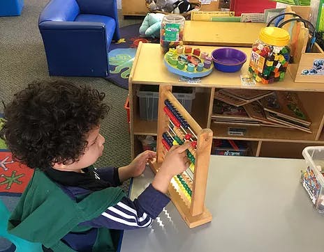 Child playing with an abacus in a classroom