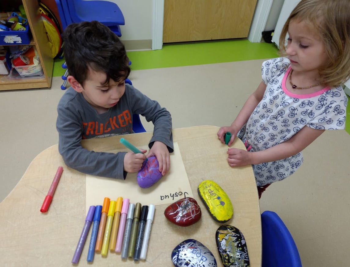 Two children decorating rocks with markers at a table