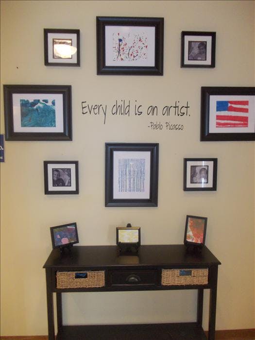 Wall decorated with framed photos and art prints, with a quote "Every child is an artist"