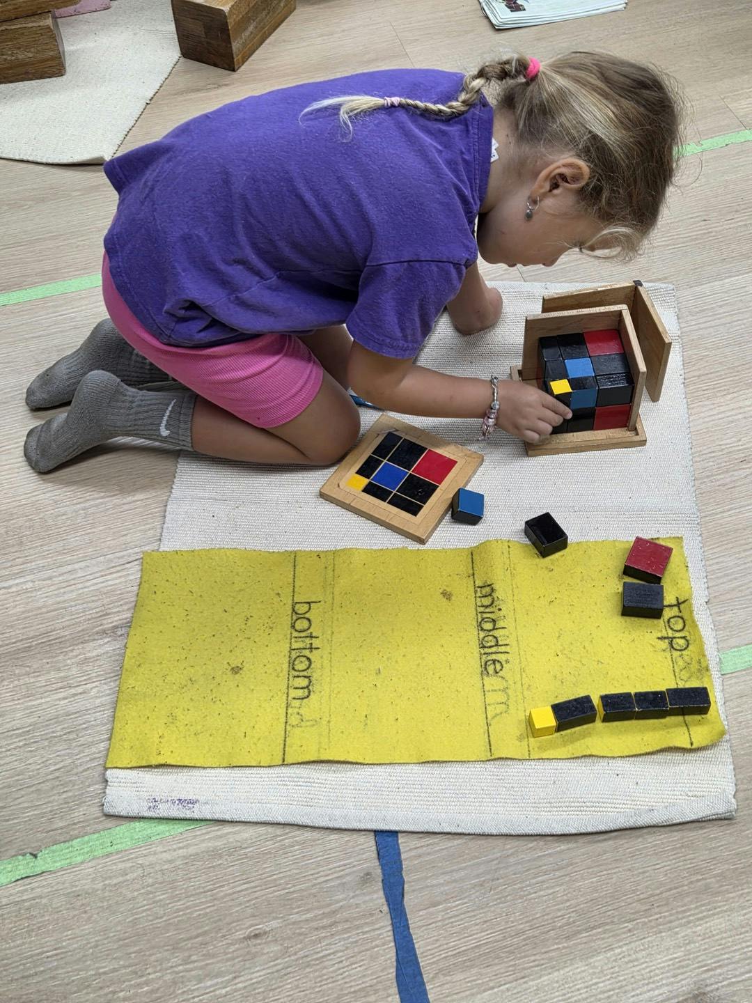Child placing colorful blocks into a wooden box on a mat labeled with positions