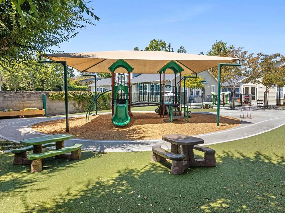 A playground with a covered structure, slide, and picnic tables