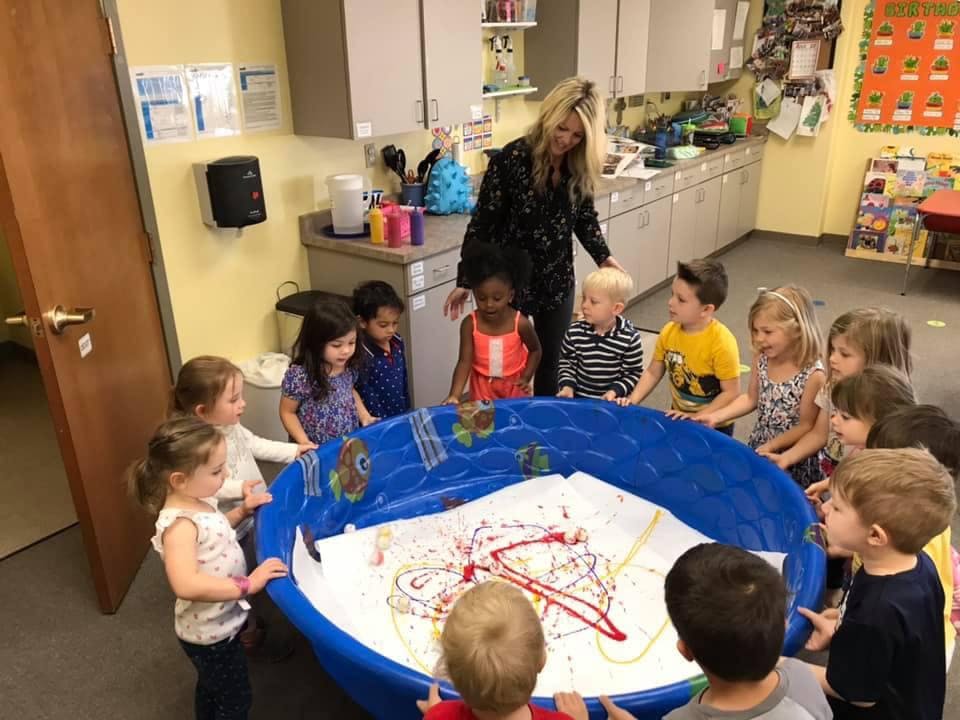 Adult and children gathered around a large blue basin with paint