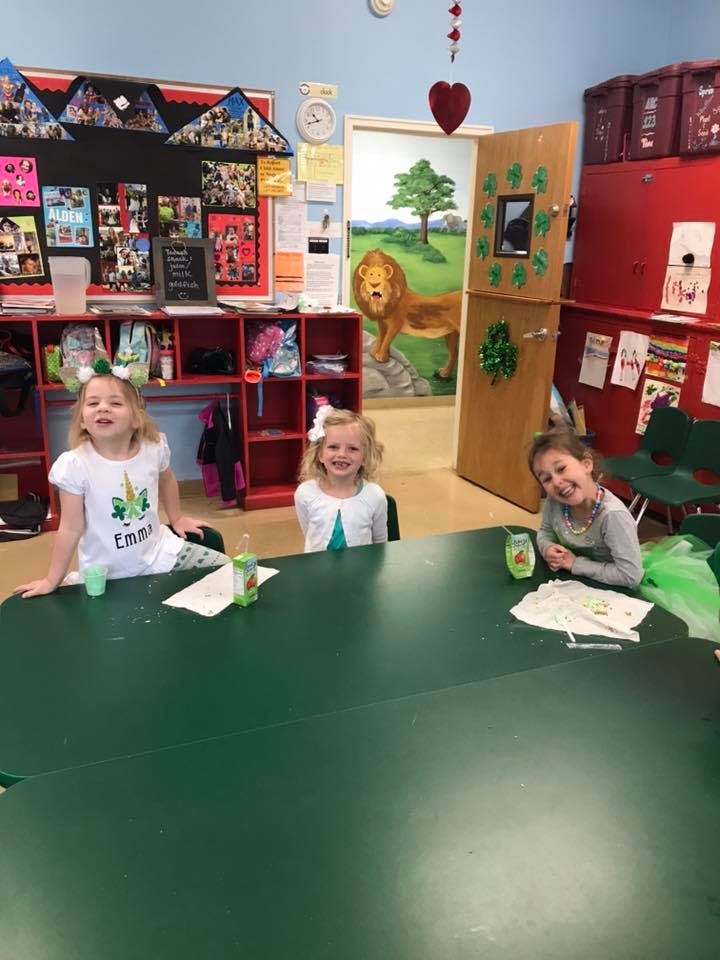 Three children sitting at a green table in a classroom