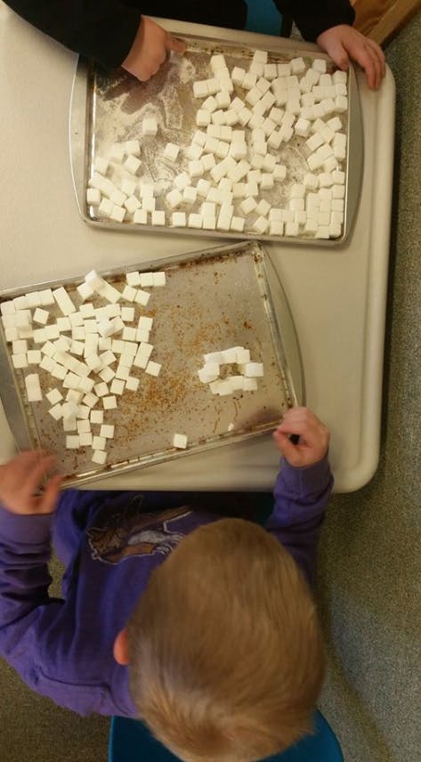 Two people playing with sugar cubes on baking sheets
