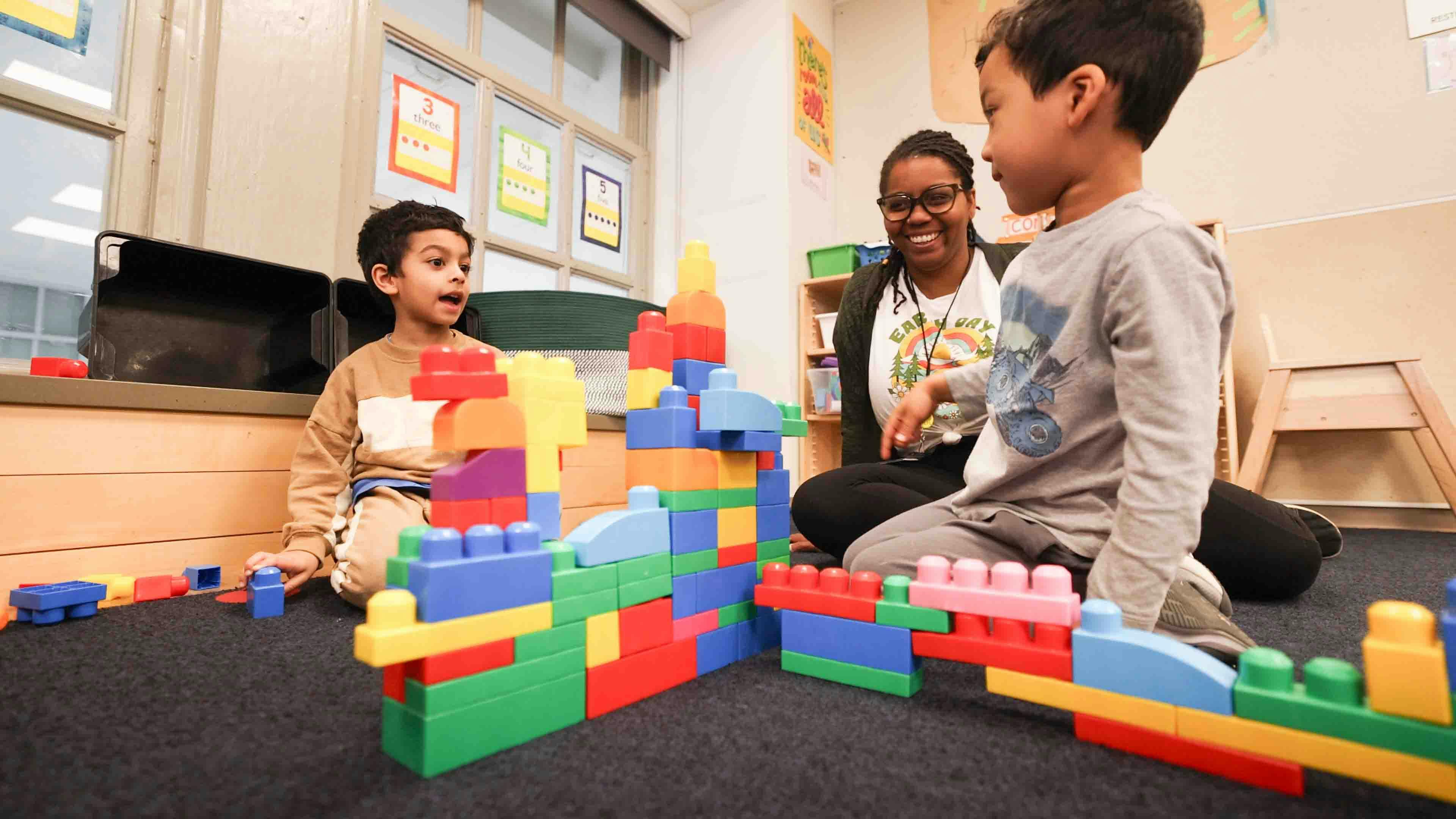 Adult and two children playing with large colorful blocks in a classroom