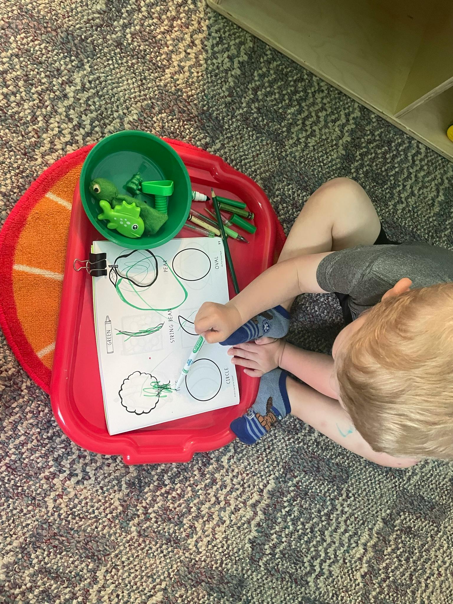 Child drawing on paper with a green marker