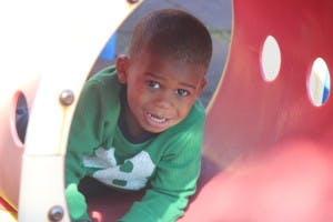 Child in a green shirt crawling through a red and tan tunnel