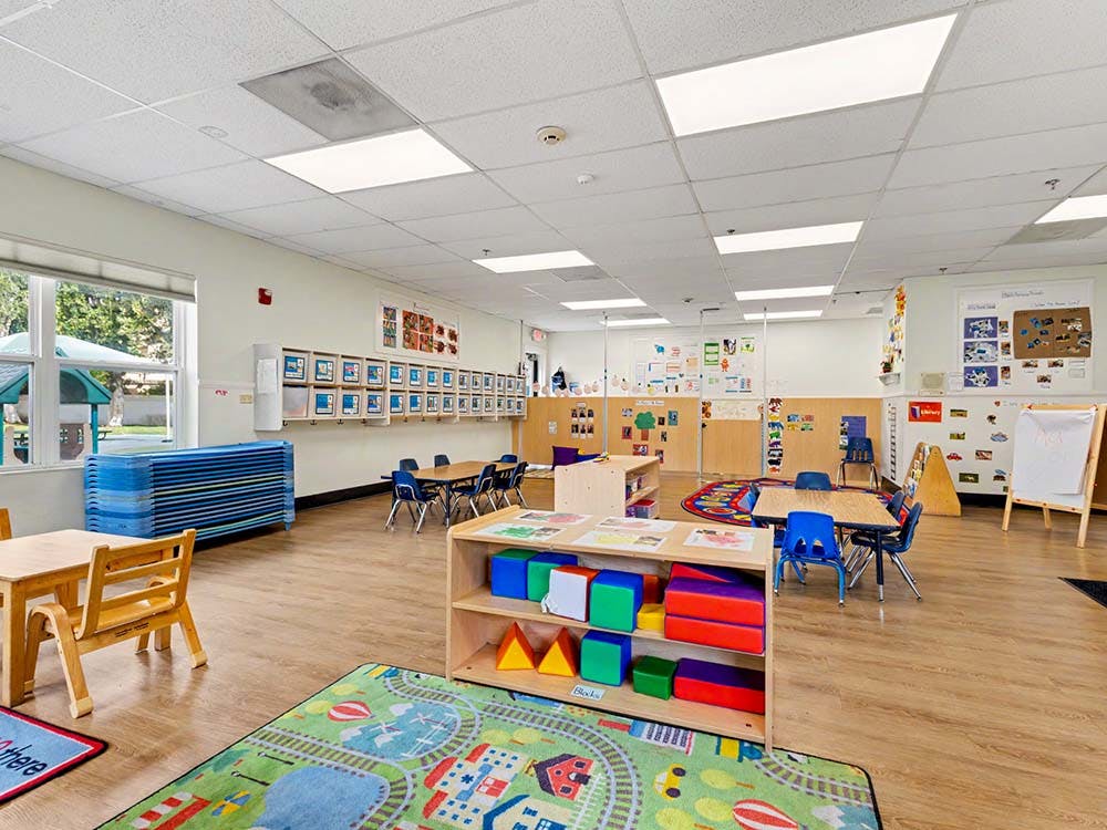 Empty colorful preschool classroom with small tables, chairs, and play mats