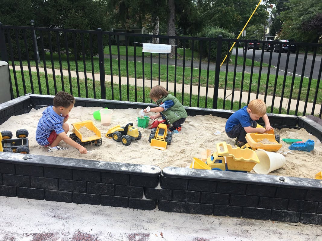 Three children playing in a sandbox with toy trucks and shovels