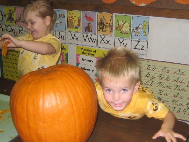 Two children with a large pumpkin in a classroom