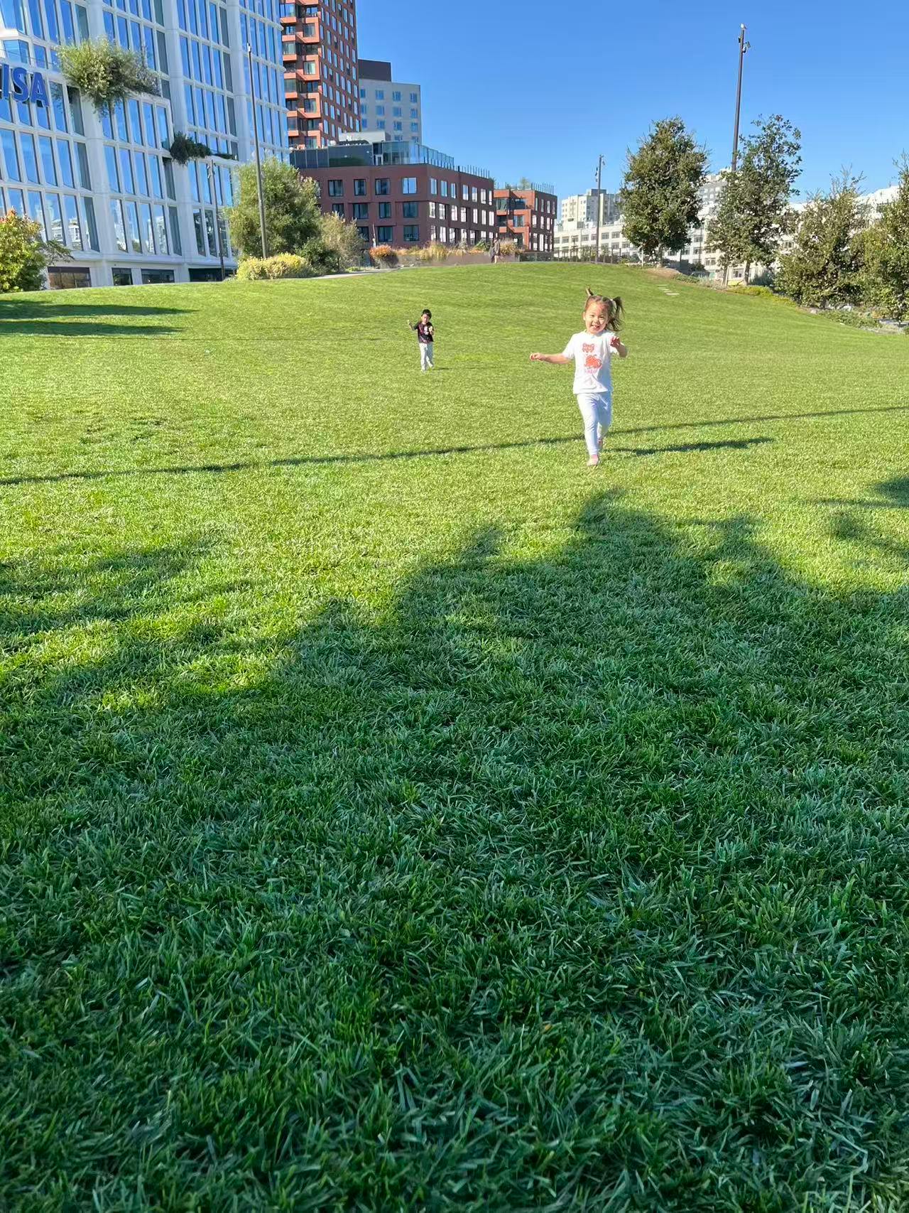 Two children running across a grassy park hill
