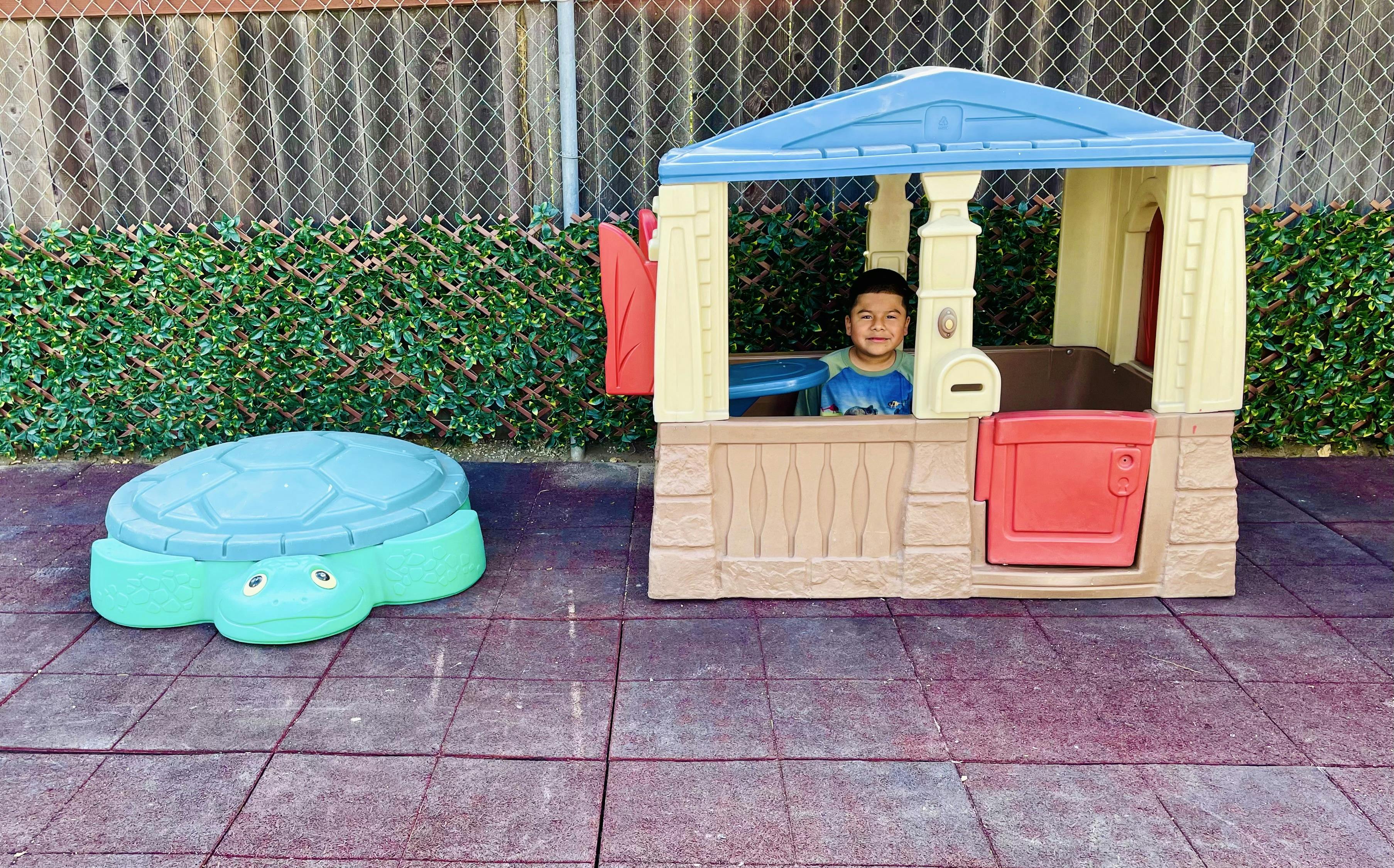 Child in a playhouse next to a turtle sandbox