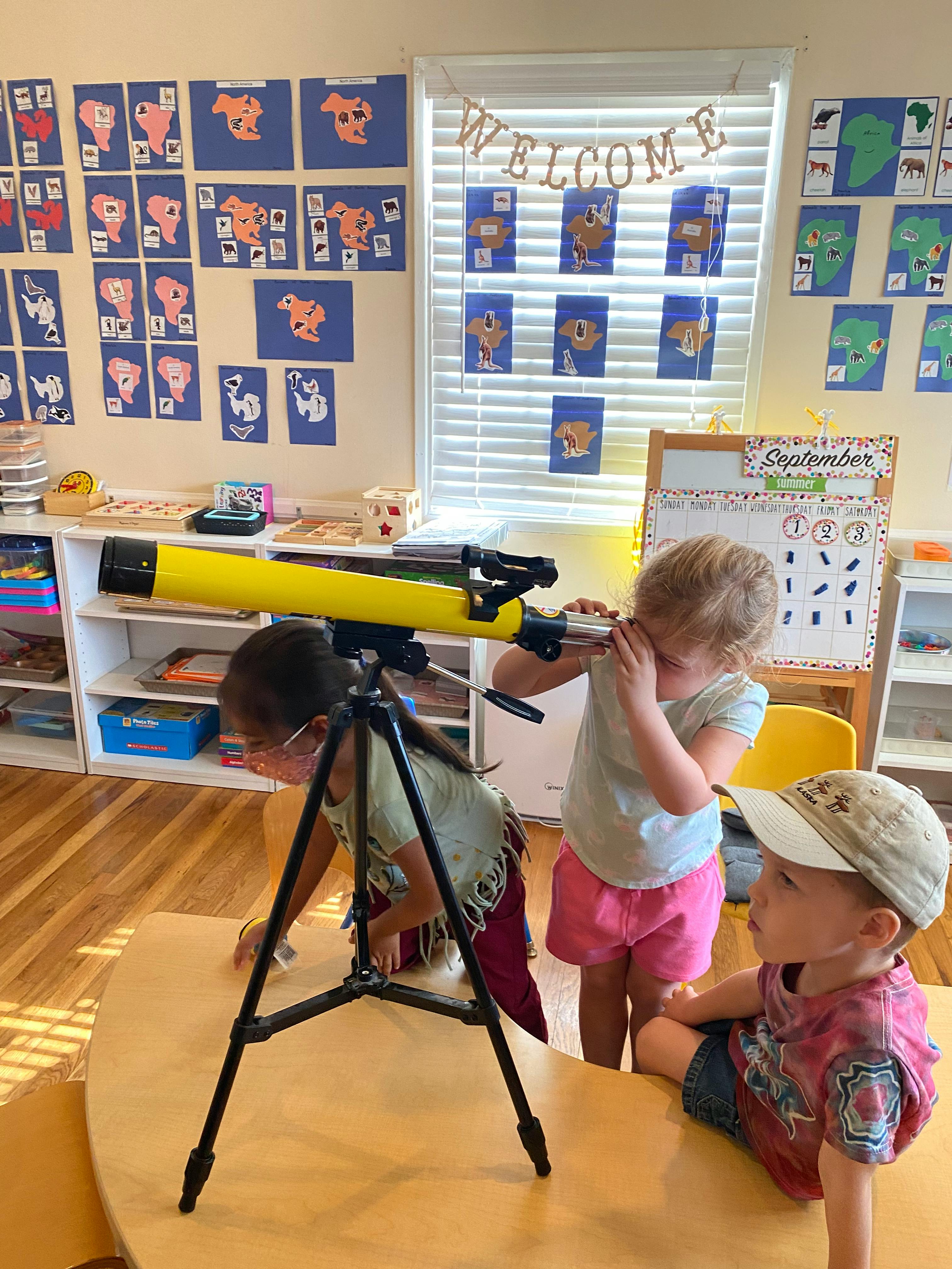 Children looking through a yellow telescope in a classroom